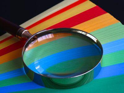 A magnifying glass sits atop a stack of coloured paper